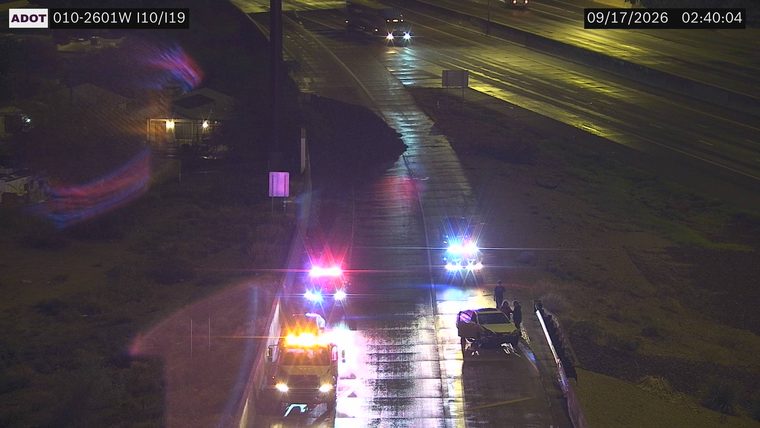 Two police cars with red and blue lights on the right shoulder, and a tow truck with amber lights in the left lane