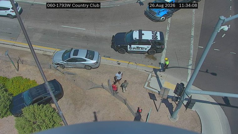 Silver sedan with visible front-end damage and deployed airbags, next to a police vehicle and several pedestrians on the roadway.