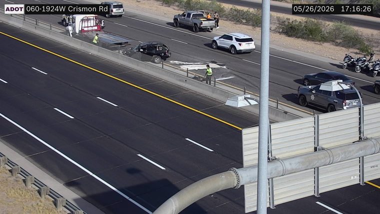 A heavily damaged SUV, a tow truck, and responders on the left shoulder/median, with a police vehicle and motorcycles on the right shoulder