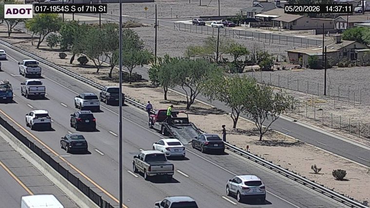 Tow truck and a disabled sedan on the right shoulder with people standing outside near the guardrail