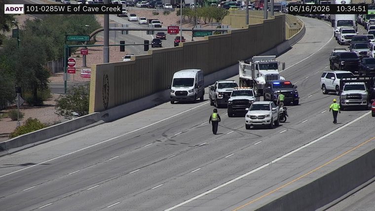 Two individuals in high-visibility vests and a police vehicle with lights on in the right lane