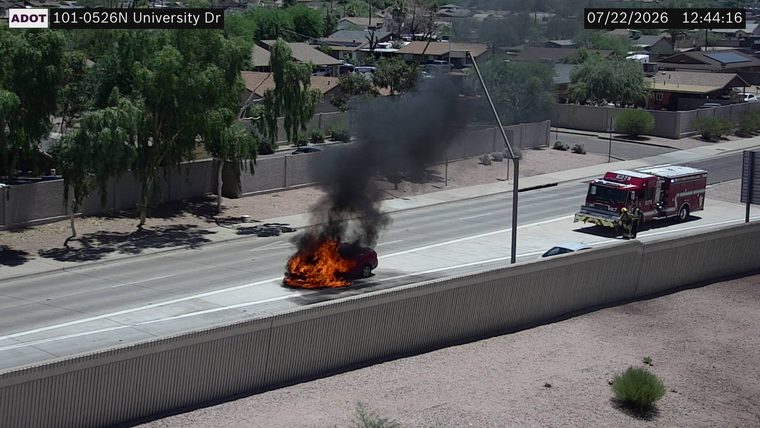 Car on fire in the right lane with a fire truck and firefighters present