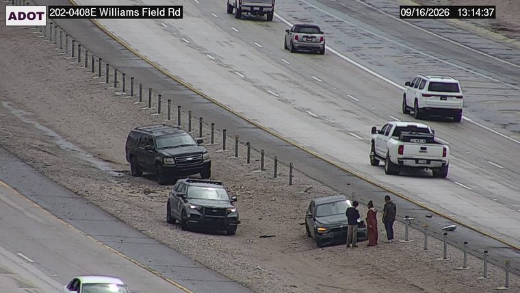 Three people standing next to a dark sedan that is off the travel lanes