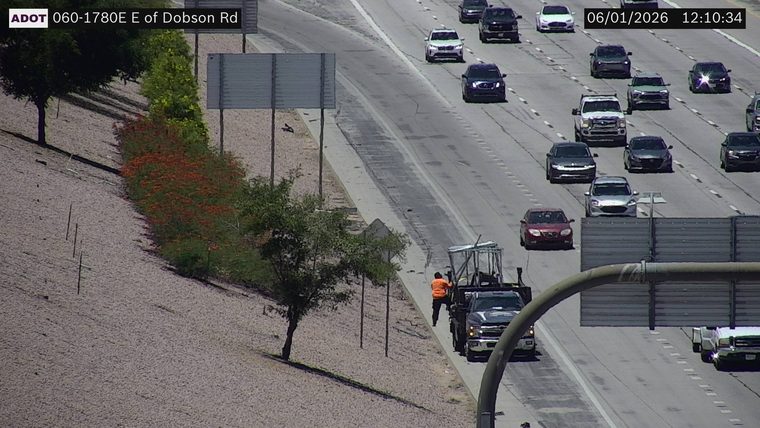 Worker in orange vest next to a truck on the right shoulder