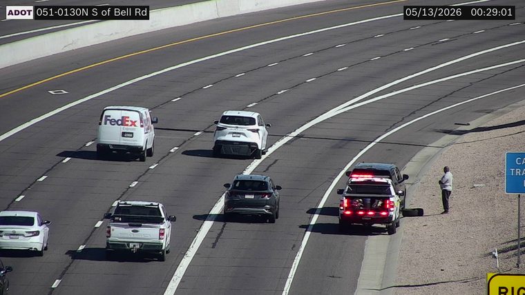 Police SUV with red and blue lights on the right shoulder, with a person standing nearby
