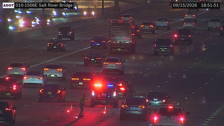 Police car with red and blue lights on, with cones and a person in the roadway