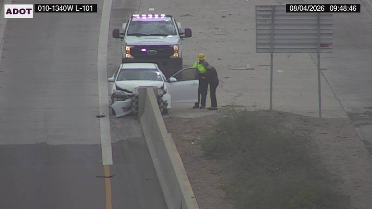 White sedan with significant front-end damage against the concrete barrier, with two individuals and a service truck nearby