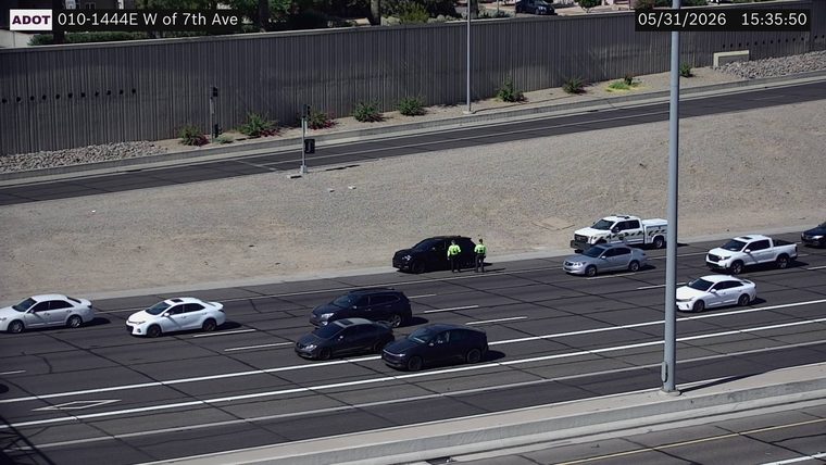Two individuals in high-visibility vests standing next to a black SUV on the right shoulder
