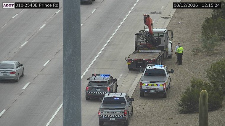 State Trooper vehicle with blue lights on the shoulder next to a flatbed truck with a crane and two individuals