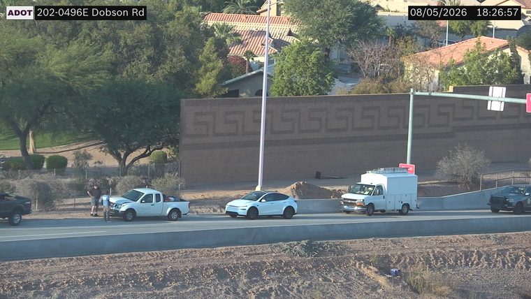 White pickup truck with visible front-end damage and two people standing near it in the right lane