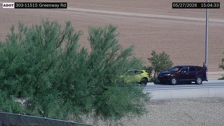 Two vehicles on the right shoulder with a person standing at the rear of the dark SUV
