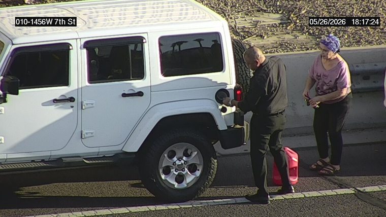 White SUV on the shoulder with two people standing outside, one pouring fuel from a red gas can