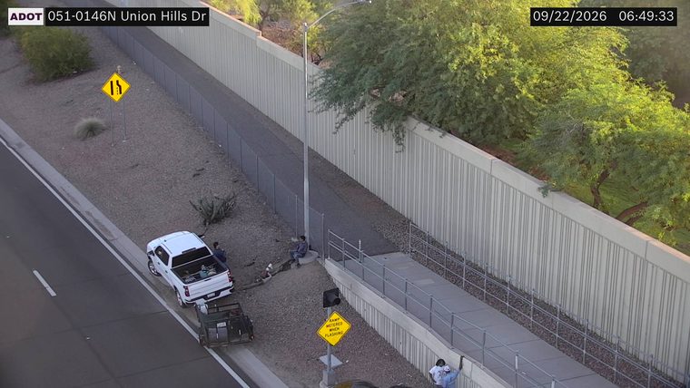 White pickup truck and trailer on the right shoulder with two people standing near it