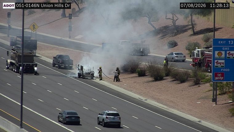 Fire and smoke from a trailer on the right shoulder, with firefighters present