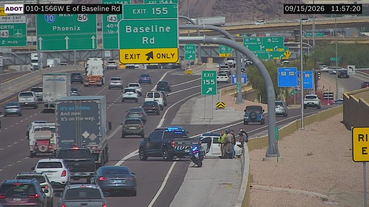 Police car and two individuals on the right shoulder next to a white vehicle