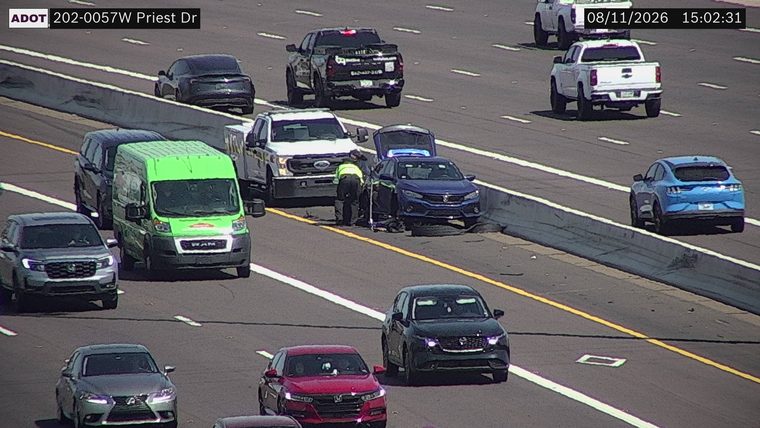 Person in hi-vis vest attending to a blue car with its hood up, next to a white truck on the right shoulder