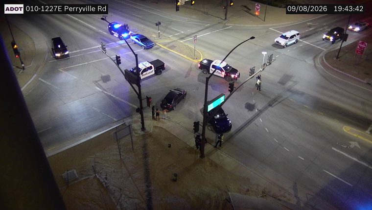 Three police cars and several individuals gathered near a black sedan in the intersection