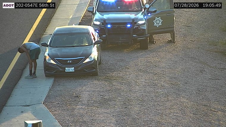 Police car with red and blue lights on the shoulder next to a stopped car