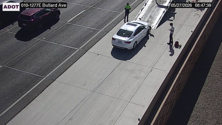 White sedan being loaded onto a tow truck on the right shoulder with two people standing nearby