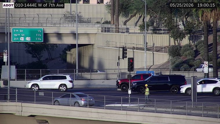 Worker in a high-visibility vest and hard hat walking on the roadway near the black SUV