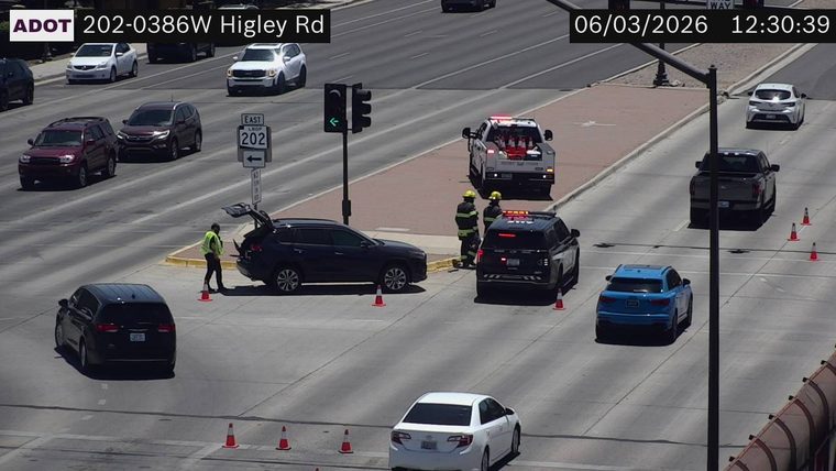 Two firefighters and a police officer attending to a dark SUV with its trunk open, with traffic cones on the roadway