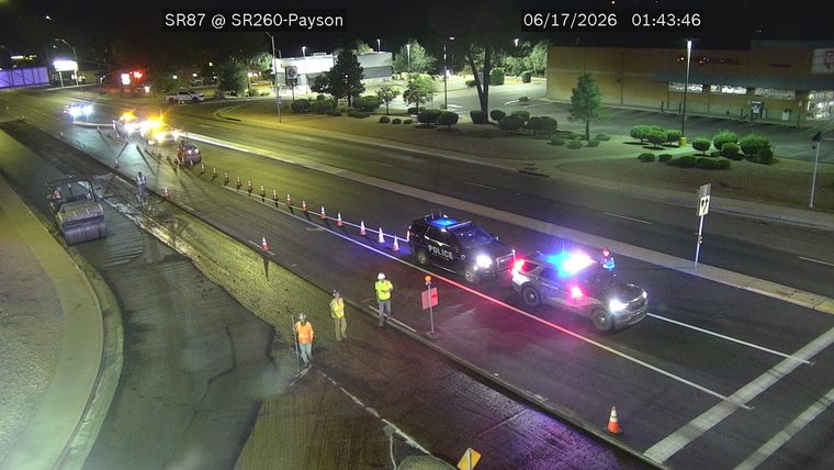 Two police cars with lights on and construction workers in the roadway
