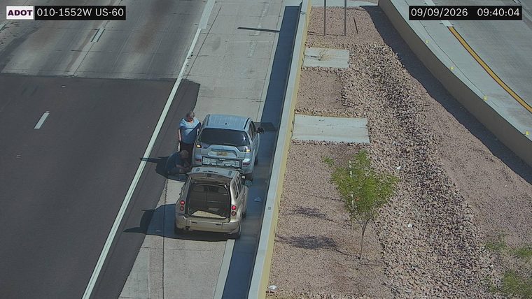 Two people attending to a silver SUV on the right shoulder