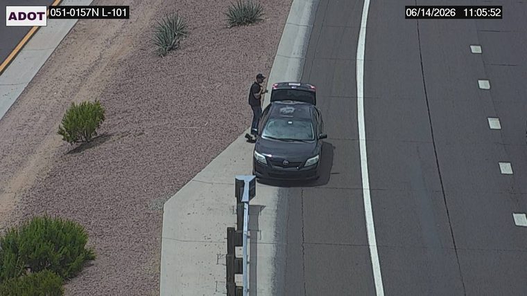 Person standing next to a car with the trunk open on the shoulder
