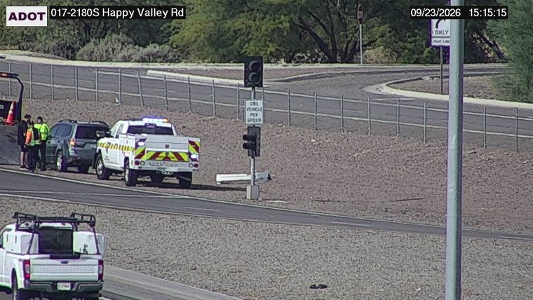 White service truck with flashing lights and two individuals standing near a dark SUV on the right shoulder