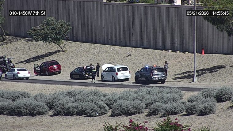 Police car with flashing lights and multiple vehicles with open doors, trunk, and hood on the right shoulder with people standing nearby
