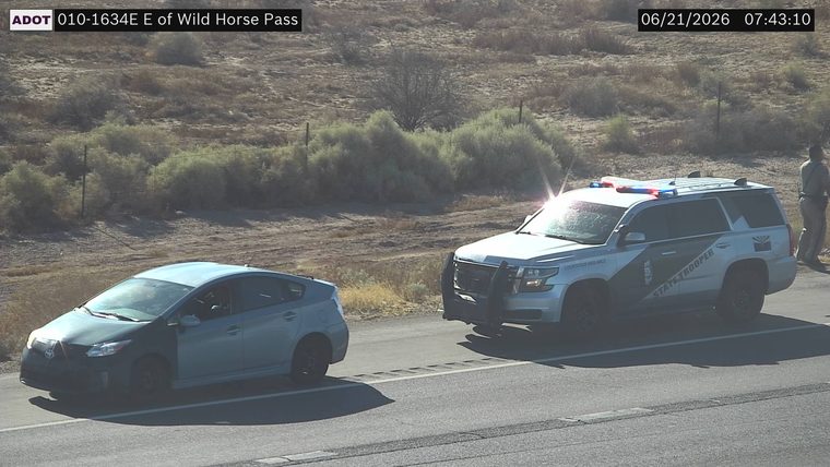 State Trooper vehicle with red and blue lights on the right shoulder, with a person standing next to it.