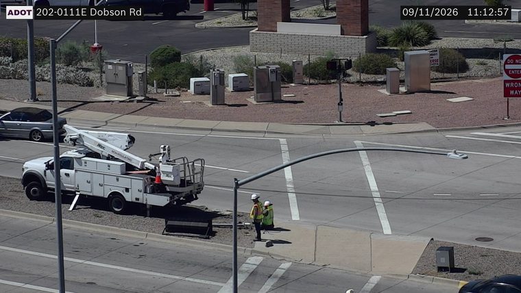 Two workers in high-visibility vests and hard hats standing near a utility truck with a boom lift on the side of the road.