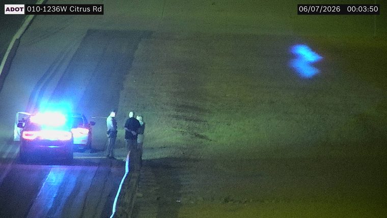 Police car with lights on the shoulder with two people standing nearby