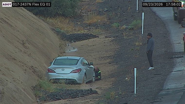 Silver sedan partially off the roadway in the dirt and mud