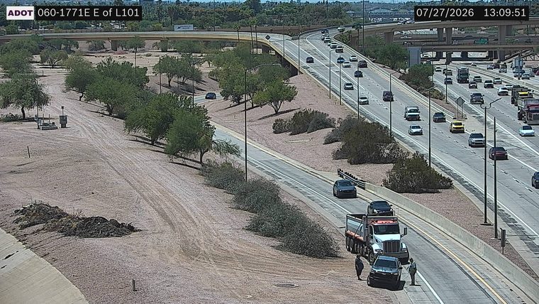 Two people standing near a dump truck and a car on the right shoulder