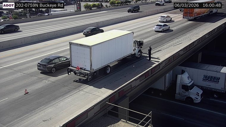 Person standing next to a white box truck with its hood open in the right lane