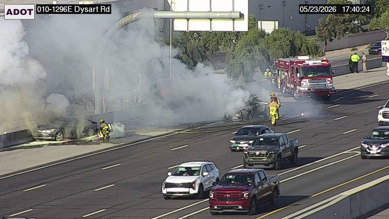 Damaged sedan crashed against the left concrete barrier, with a fire truck and emergency responders on the right shoulder