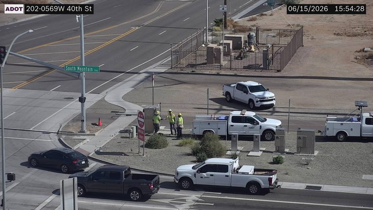 Three construction workers and two white trucks near a utility box