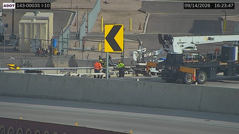Two workers with high-visibility vests and hard hats near construction equipment and a truck on the side of the road