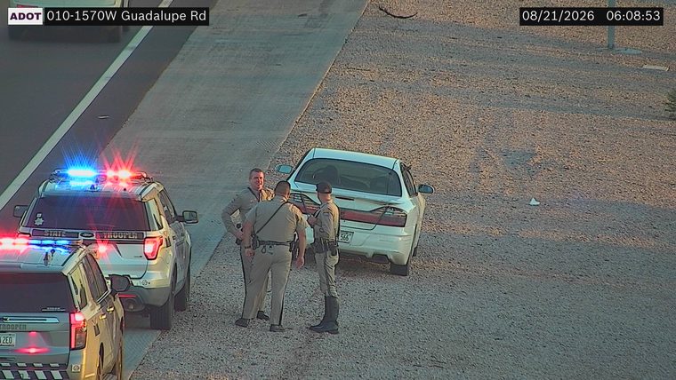 Two state trooper vehicles with lights on and three officers by a white sedan on the shoulder