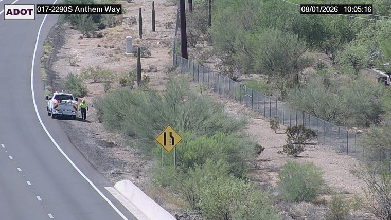 Tow truck with hazard lights on and a person standing beside it on the right shoulder