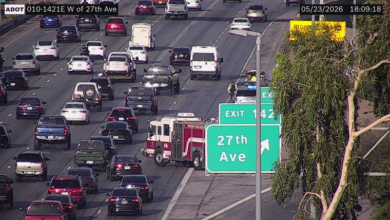 Fire truck and police vehicle with flashing lights on the right shoulder/exit gore area near the 27th Ave exit sign