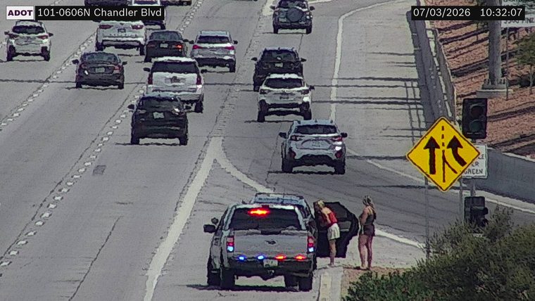 Police car with red and blue lights on the shoulder with two people standing nearby
