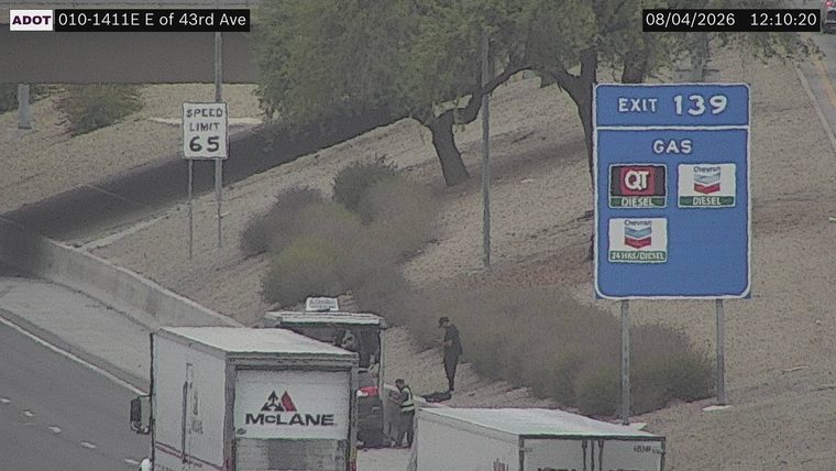 Two people are attending to a white van on the right shoulder, with a large cloud of dust or smoke behind it.