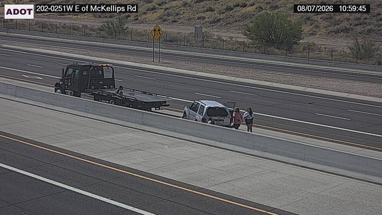 Tow truck assisting a silver SUV on the right shoulder, with three people standing nearby