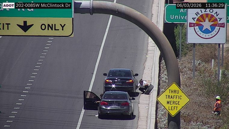 Person changing tire on the right shoulder next to a dark sedan