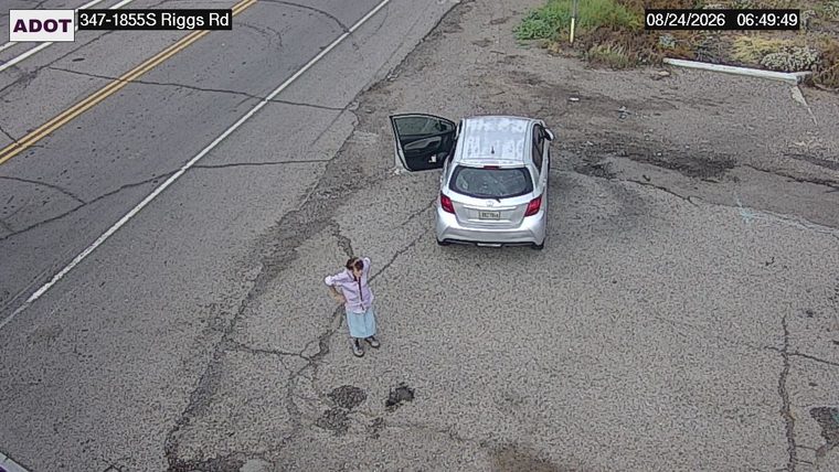 Silver car with driver's door open and a person standing next to it off the travel lanes