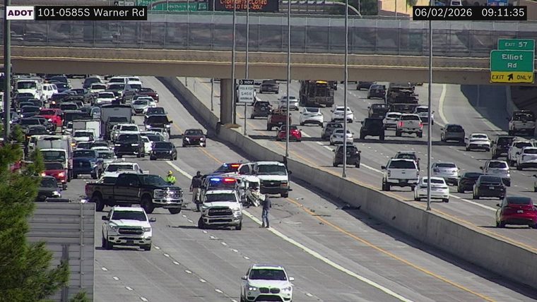 Police car with lights on in the left lane, with two people standing nearby and debris in the roadway