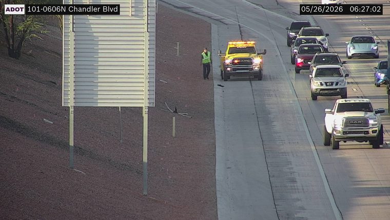 Yellow service truck with flashing lights and a worker in a high-visibility vest on the left shoulder