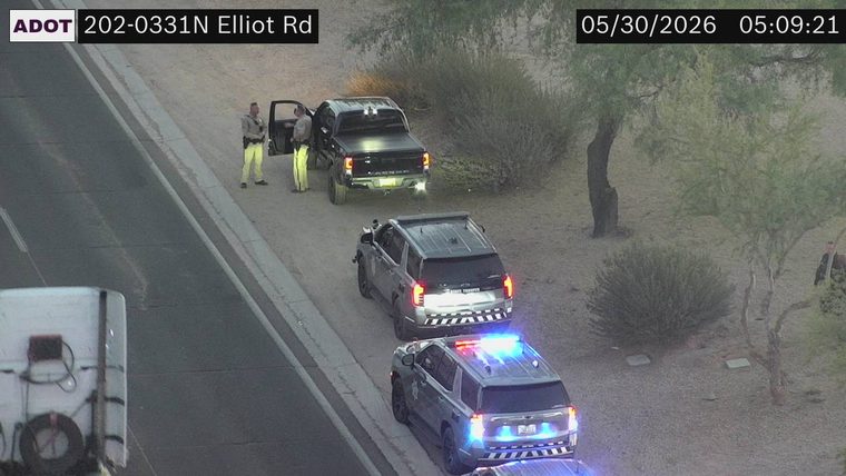 Two police vehicles with lights on and two officers interacting with a pickup truck on the right shoulder